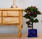 1:12 scale miniature flowering tree with pink blossoms in a square blue pot, shown beside a wood dresser