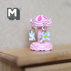 1:12 scale miniature carousel merry go round in pink with hanging pastel horses, shown on a wood dresser