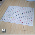 1:12 scale miniature multicolor dot shag rug in white, rectangular with rows of colored dots, shown on a wood floor