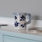 1:12 scale miniature ceramic jug in blue and white with hand painted blue leaf pattern, shown beside a coin