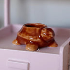 1:12 scale miniature ceramic turtle planter in glossy brown, shown empty on a pink cabinet
