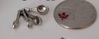 1:12 scale miniature metal measuring spoons in silver on a ring, set of 4, shown beside a coin for scale