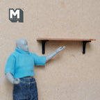 1:12 scale miniature floating wall shelf with black brackets, natural wood tone, shown on a wall beside a posable figure