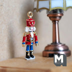 1:12 scale miniature metal nutcracker soldier ornament in red and blue with a hanging loop, shown beside a table lamp