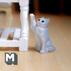 1:12 scale miniature sitting cat with paw up in gray, shown reaching toward a white table leg