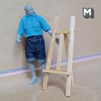 1:12 scale miniature wood painting easel stand in natural finish, tall tripod style shown beside a posable figure