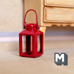 1:12 scale miniature metal camping lantern in red with a wire carry handle and open sides, shown on the floor