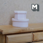 1:12 scale miniature gift boxes with lids in light pink, oval and round, set of 2, shown stacked on a wood dresser