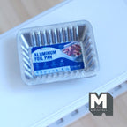 1:12 scale miniature foil style roasting pan in silver, large, ribbed sides with a blue printed label, on a white table