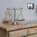 1:12 scale miniature metal balance scale in champagne gold with weights and tweezers, non working, on a wood dresser
