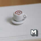 1:12 scale miniature hot chocolate cup with saucer, white cup with a brown swirl top, shown on a white table