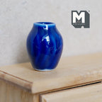 1:12 scale miniature ceramic plum vase in dark blue with a glossy glaze and rounded body, shown on a wood dresser