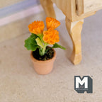1:12 scale miniature potted orange carnations in a clay pot with green leaves, shown on the floor beside furniture