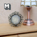1:12 scale miniature round metal portrait frame with stand in antique bronze, filigree loop border, shown beside a table lamp