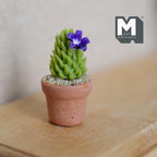 1:12 scale miniature potted cactus with purple flower, green ridged cactus in a clay pot, shown on a wood dresser