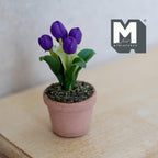 1:12 scale miniature potted tulips in deep purple in a clay pot with green leaves, shown on a wood dresser