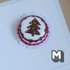 1:12 scale miniature Christmas tree cake in white with red trim and a chocolate tree on top, shown on a lace doily