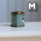 1:12 scale miniature octagonal tea tin with lid in green with a printed label and copper tone lid, on a white table