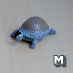 1:12 scale miniature garden tortoise in cast resin, blue body with a gray patterned shell, shown on a light wood surface