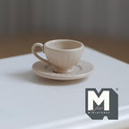 1:12 scale miniature coffee cup and ribbed saucer in beige, set of 2, fluted cup with handle on a white table