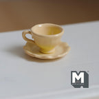1:12 scale miniature tea cup and scalloped saucer in yellow, set of 2, flared cup with handle on a white table