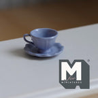 1:12 scale miniature tea cup and scalloped saucer in lavender, set of 2, flared cup with handle on a white table