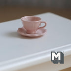 1:12 scale miniature tea cup and scalloped saucer in pink, set of 2, flared cup with handle on a white table