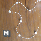 1:12 scale miniature pearl bead garland chain in white with large and small beads, shown looped on a wood surface