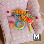1:12 scale miniature rainbow knitting project with wood needles and a loop of rainbow yarn, shown on a pink armchair