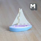 1:12 scale miniature toy sailboat with a beige sail and mast, light blue hull with lilac deck, on a wood surface
