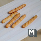 1:12 scale miniature baguettes, set of 5, golden brown loaves with scored tops, shown on a light wood table