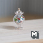 1:12 scale miniature glass apothecary jar with gumballs and fixed lid, clear footed jar with colorful candy, on a wood table