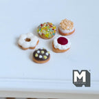 1:12 scale miniature glazed donuts, set of 5, white, green and chocolate icing with sprinkles and jam, on a white table