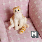 1:12 scale miniature Scottish fold tabby cat sitting up, orange and white with a striped tail, shown on a pink armchair