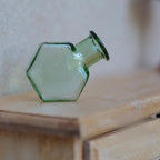 1:12 scale miniature hexagon glass bottle vase in translucent green, shown lying on its side on a wood dresser