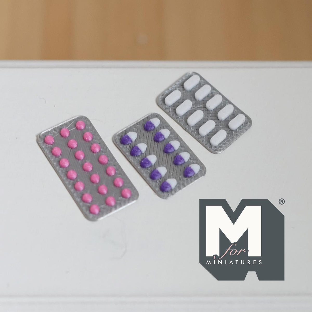1:12 scale miniature pill blister packs, set of 3, silver foil with pink, purple and white pills, on a white surface