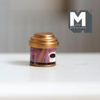 1:12 scale miniature round coffee tin with lid, style B, pink and purple print with a gold tone lid, on a white table