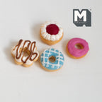 1:12 scale miniature glazed donuts, set of 4, pink and blue icing with chocolate drizzle and jam, on a white table