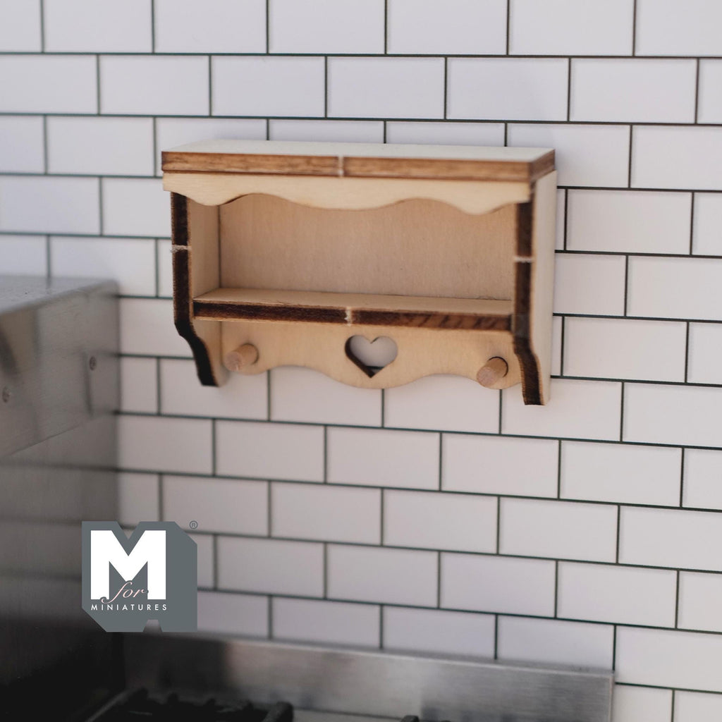 1:12 scale miniature wood heart cutout wall shelf kit with 2 coat pegs, shown assembled on a white tile wall