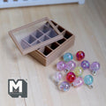 1:12 scale miniature glass Christmas baubles in pastel pink, lavender, aqua, red, clear and yellow with an iridescent shine, in a tan storage box with a clear lid