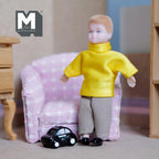 1:12 scale miniature toy police car in black and white, shown on the floor beside a boy doll and a pink armchair
