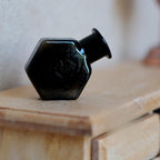 1:12 scale miniature hexagon glass bottle vase in black, shown lying on its side on a wood dresser