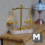1:12 scale miniature T beam balance scale in gold with hanging pans and weights on a wood base, on a dresser