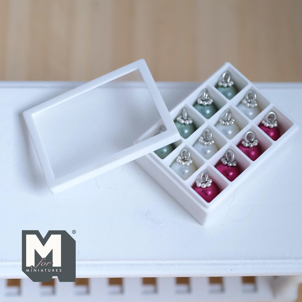 1:12 scale miniature Christmas baubles in sage green, pearl white and magenta pink with silver caps, in a white 12 compartment storage box