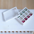 1:12 scale miniature Christmas baubles in sage green, pearl white and magenta pink with silver caps, in a white 12 compartment storage box
