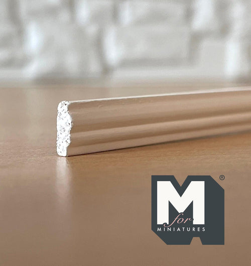 1:12 scale miniature beaded wainscot wood rail in white, close view of the molded profile end on a wood surface