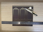 1:12 scale miniature embossed boiserie wallpaper in charcoal with gold foil panels, shown with a ruler and craft knife