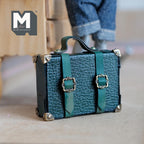 1:12 scale miniature dark green pebbled faux leather suitcase with two buckle straps, metal corner caps and a strap handle on top