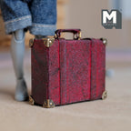 1:12 scale miniature burgundy faux leather suitcase with a worn distressed finish, two buckle straps, metal corner caps and a top handle on metal rings