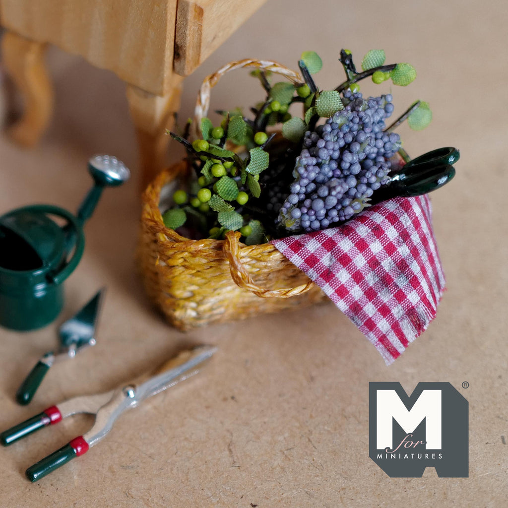 Miniature grape harvest basket set on the floor beside a green watering can and garden tools